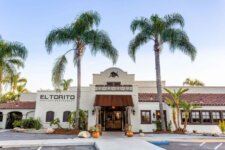 Exterior view of El Torito Mexican Restaurant with a white stucco facade, brown awning, and tall palm trees framing the entrance