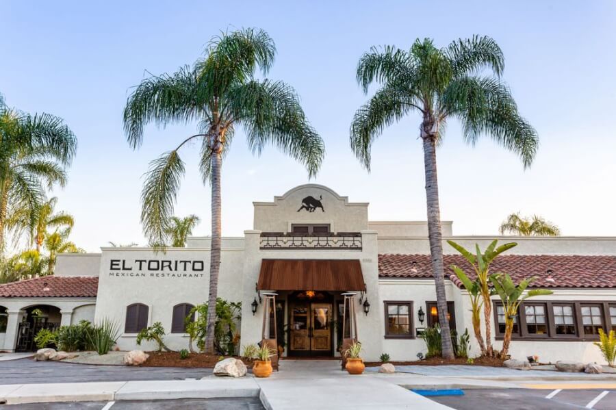 Exterior view of El Torito Mexican Restaurant with a white stucco facade, brown awning, and tall palm trees framing the entrance