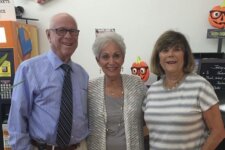 Three seniors pose indoors with Halloween decorations behind them; left: man in a blue striped shirt and tie, center: woman in a light cardigan, right: woman in a striped gray top.