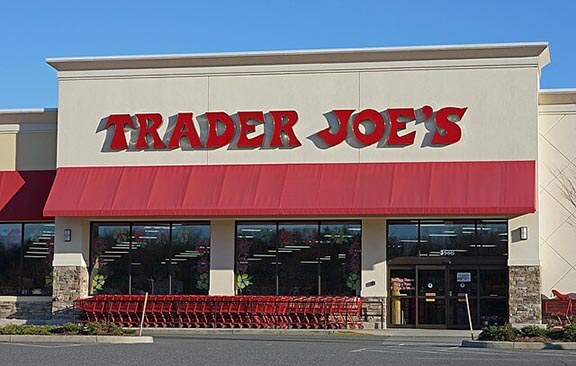 Exterior of a Trader Joe's store with a red awning and shopping carts outside the entrance. This is the storefront signage and facade of a grocery store.