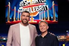 Two men pose on a TV game show stage with a bright 'Are You Smarter Than a Celebrity' banner behind them, smiling.