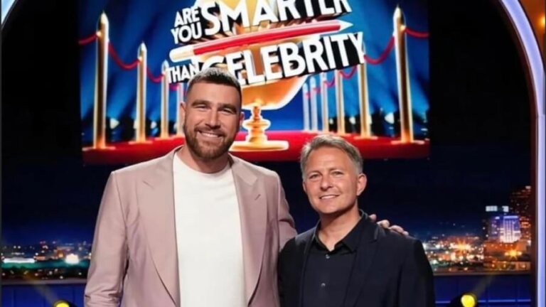 Two men pose on a TV game show stage with a bright 'Are You Smarter Than a Celebrity' banner behind them, smiling.