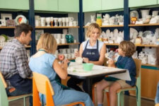 Instructor at Color Me Mine guides a pottery-painting class with kids and adults around a table with ceramic pieces in the background.