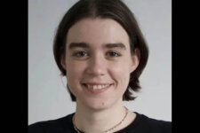 Portrait of a young woman (Jane Wickline) with short brown hair, smiling and wearing a dark top and a thin necklace.