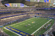Wide view of Sofi stadium during a football game, with a large video screen overhead and players on the field.