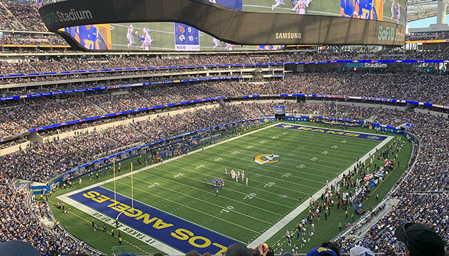 Wide view of Sofi stadium during a football game, with a large video screen overhead and players on the field.