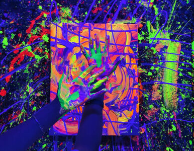 Hands covered in neon purple, green, and pink paint press onto a swirled orange canvas in a vivid abstract painting scene, with splatters around.