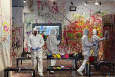 Splatter Studio LA painting | Santa Monica Sun People in white protective suits and gloves painting a wall covered in colorful splatters in a paint-splatter art studio.