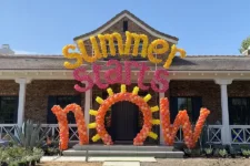 Balloon Celebrations - summer | Santa Monica Sun Front porch of a brick house with a balloon display reading 'Summer starts now' in yellow and pink, with sun-shaped balloons nearby.