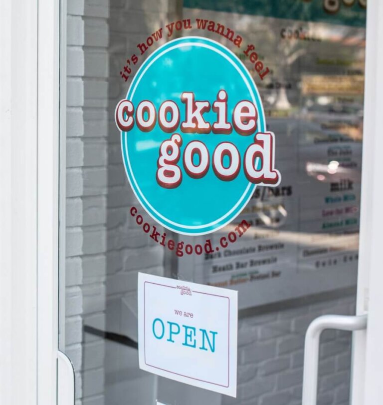 Storefront door with a teal circular 'cookie good' logo on the glass and an "OPEN" sign in blue text below it.