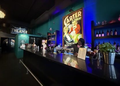 Bar counter inside a theater lobby with a bartender serving drinks and a large vintage Carter poster behind him.