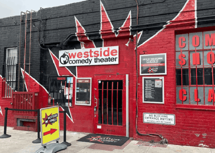 Exterior of Westside Comedy Theater building with a red/black mural, entrance door, and ticket signs visible on the wall.”,