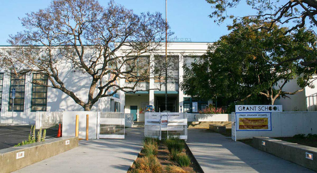 Front view of Grant School with a paved courtyard, banners, and a large tree in front.