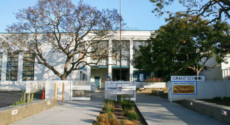 Front view of Grant School with a paved courtyard, banners, and a large tree in front.