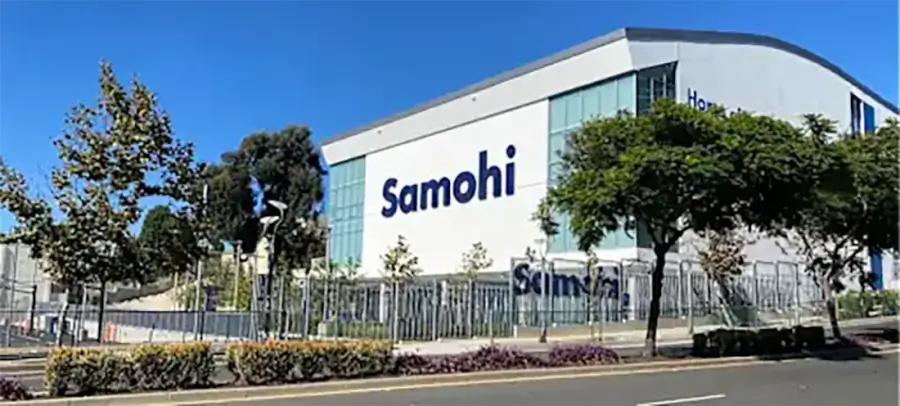 Exterior of a modern high school building with a large 'Samohi' sign, fenced grounds and trees.