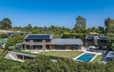 Modern two-story home with solar panels, a spacious lawn, and a rectangular pool in the backyard.