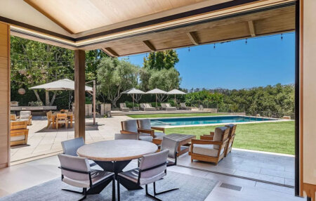 859 Woodacres Road - interior | Santa Monica Sun Open patio overlooking a rectangular pool with lounge chairs, umbrellas, and a lush green landscape beyond the deck.