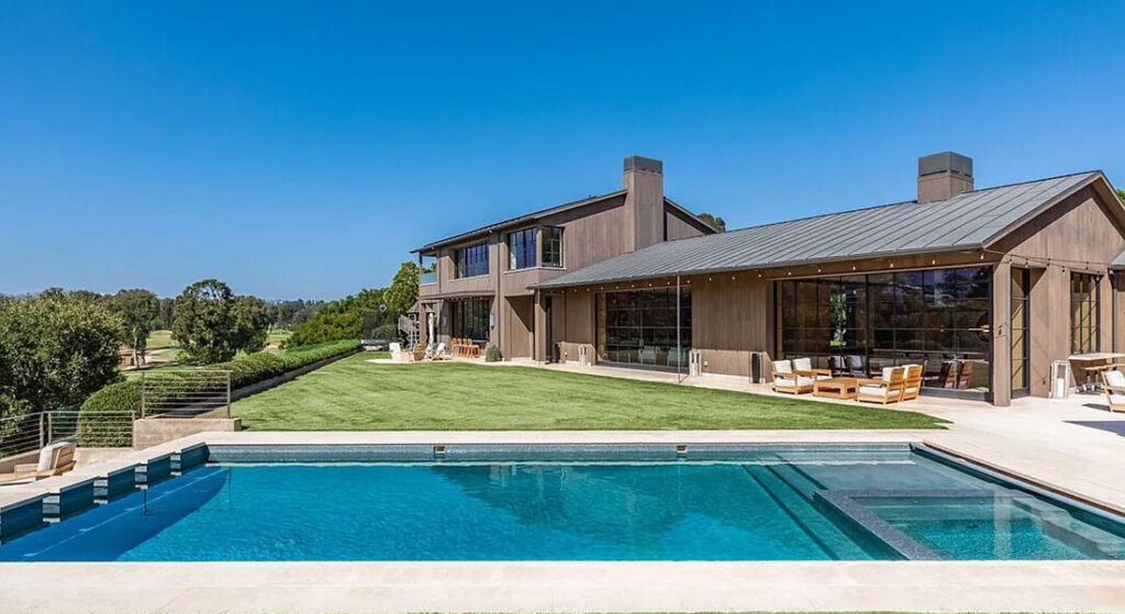 Contemporary two-story home with large glass walls, wood siding, and a rectangular pool in a sunny backyard.