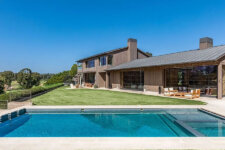 Contemporary two-story home with large glass walls, wood siding, and a rectangular pool in a sunny backyard.
