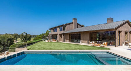 Contemporary two-story home with large glass walls, wood siding, and a rectangular pool in a sunny backyard.