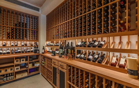 859 Woodacres Road wine cellar | Santa Monica Sun Wooden-wine rack-filled cellar with bottles along walls and a long counter displaying spirits.