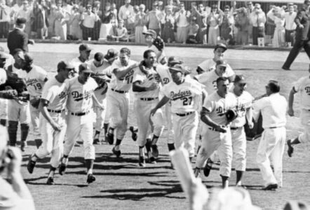 Dodgers players celebrate on the field with fans applauding in the background, black-and-white photo.