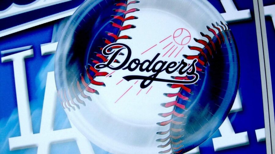 Dodgers logo on a baseball with red stitching, blue stadium background behind it