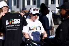 Volunteers at an outdoor event distribute T-shirts, one woman proudly holding a black shirt for a Delta Airlines volunteer program.