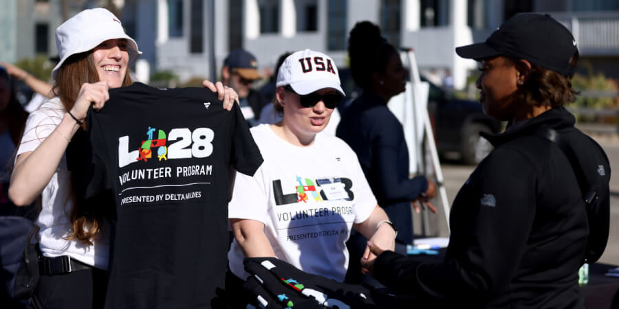 Volunteers at an outdoor event distribute T-shirts, one woman proudly holding a black shirt for a Delta Airlines volunteer program.
