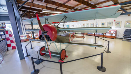 Vintage biplane on display in a museum hangar, red nose and propeller in view.