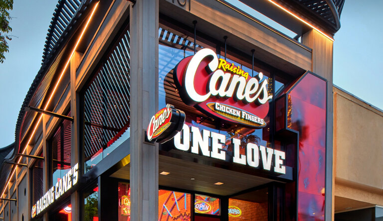 Exterior of a Raising Cane's restaurant with large illuminated 'Cane's' logo and 'ONE LOVE' sign on the storefront.