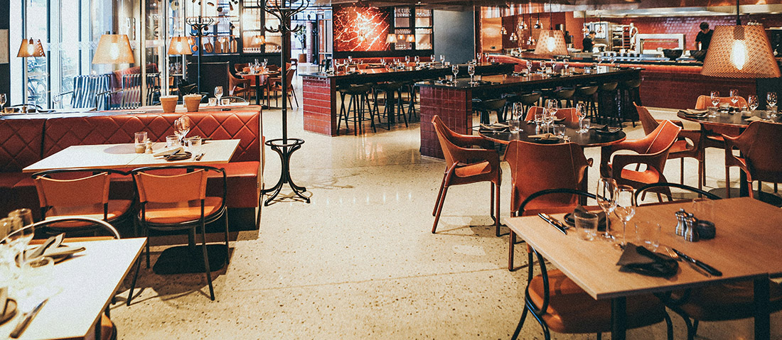 Cozy restaurant dining area with orange chairs, wooden tables, and warm pendant lighting.