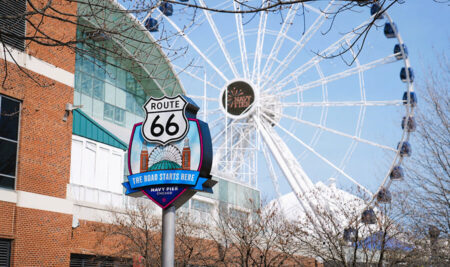 Route 66 sign at Navy Pier with a large Ferris wheel in the background on a clear day in Chicago, IL.