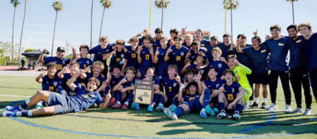 Youth soccer team poses on field after championship, holding a plaque and celebrating together under palm trees.