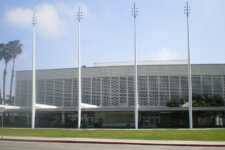 Public building with a perforated brick facade, seven flagpoles in front, and palm trees on a manicured lawn.