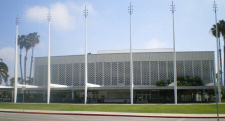 Public building with a perforated brick facade, seven flagpoles in front, and palm trees on a manicured lawn.