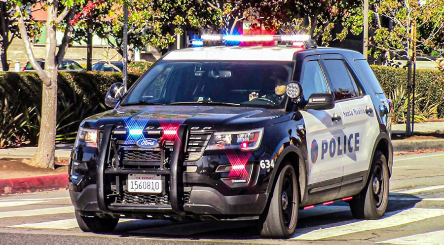 Police SUV with flashing red and blue lights driving on a street; Santa Monica Police markings on the side (POLICE).