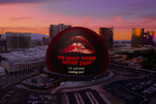 Large red lips logo on a dark spherical building at Las Vegas Sphere, sunset skyline in the background.