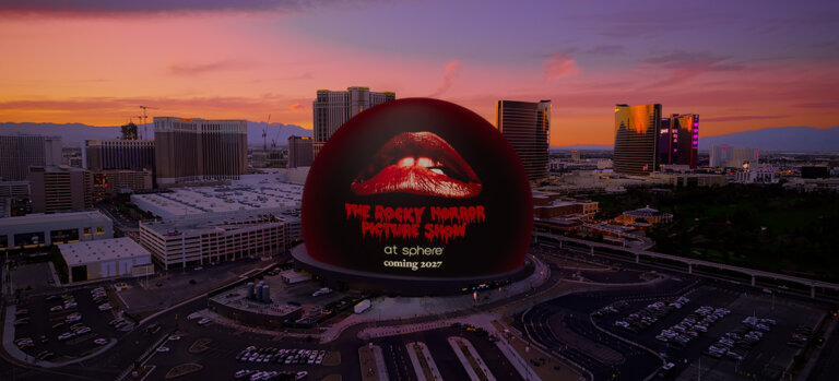 Large red lips logo on a dark spherical building at Las Vegas Sphere, sunset skyline in the background.