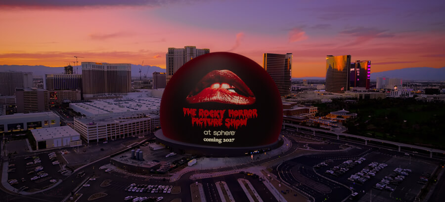 Large red lips logo on a dark spherical building at Las Vegas Sphere, sunset skyline in the background.