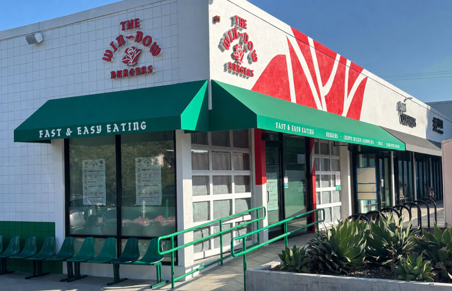 Storefront of a fast-food restaurant with green awnings saying 'Fast & Easy Eating', outdoor seating, and a wheelchair ramp outside.