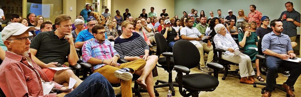 Large audience seated in a conference room, listening to a presentation in progress.