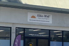 Exterior of Elder-Well Adult Day Program center with glass storefront and sign above entrance.