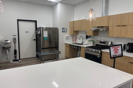 Break room with white island, stainless fridge, sink and stove along the wall, and a sign reads 'Employees Beyond This Point'.