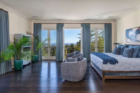 Bright hotel bedroom with a king bed, blue bedding, and balcony doors opening to an ocean view.