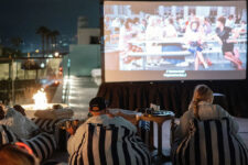 Group of people lounging on striped bean bags watching a movie on a rooftop projector screen at night