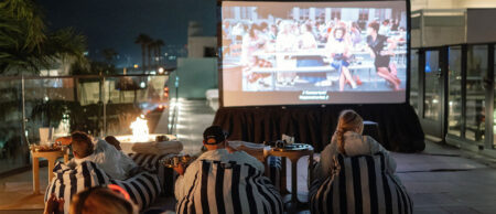 Group of people lounging on striped bean bags watching a movie on a rooftop projector screen at night