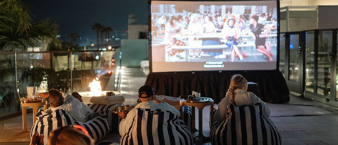 Group of people lounging on striped bean bags watching a movie on a rooftop projector screen at night