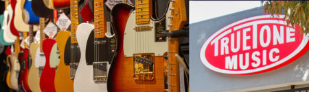 Row of colorful electric guitars on display in a music store, with a sunburst guitar in the foreground and a True Tone Music sign on the right.