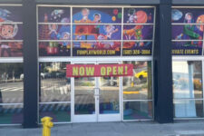 Storefront of a children's play center called Fun Play World with colorful cartoon banners in the windows and a large 'NOW OPEN!' sign above the entrance.